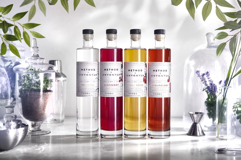 Four tall, slender glass bottles with varied liquor inside. Surrounded with cloches with fresh herbs.